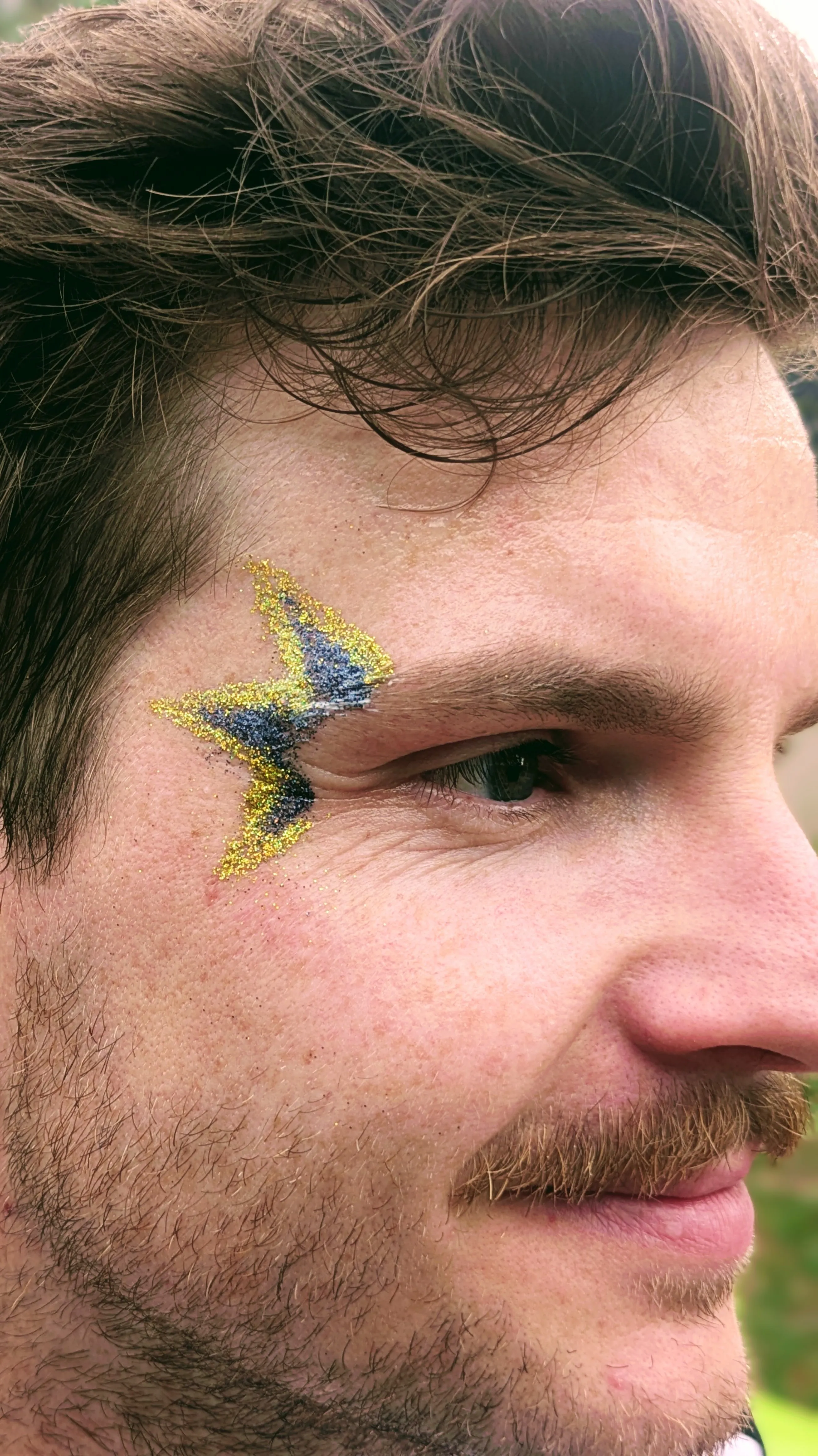 Maquillage glitter dor&eacute; et bleu en forme d&rsquo;&eacute;clair autour de l&rsquo;&oelig;il d&rsquo;un homme